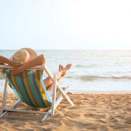 Person mit Hut liegt am Stand im Sonnenstuhl