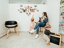 Junge Mutter sitzt im Wartezimmer mit Baby auf dem Arm und Sohn der auf dem Boden spielt